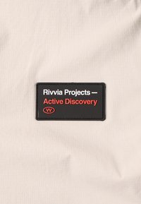 Tessuto grigio con un'etichetta rettangolare nera con testo bianco e rosso che recita "Rivvia Projects — Active Discovery."