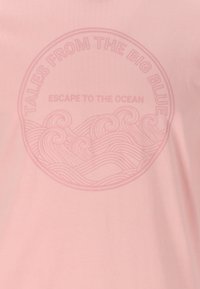 Vaaleanpunainen t-paita, jossa on pyöreä graafinen kuvasto meriaalloista ja tekstit: "Tarinoita Suuresta Sinisestä" ja "Pakeneminen Merelle."