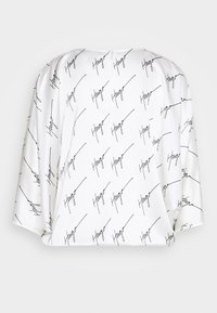 Blusa bianca con testo "Hugo" nero ripetuto, maniche corte, vestibilità rilassata e chiusura a bottone sul retro. Tessuto dalla consistenza liscia.