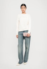 Krémová mikina s vyraženým logem "Armani Exchange", v kombinaci s džínami s širokým střihem v světle modré barvě. Růžová kabelka a bílé špičaté boty.