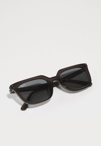 Ochelari de soare Ray-Ban cu un cadru din plastic de culoare maro închis, formă pătrată și lentile închise la culoare. Prezentă logo pe lentila stângă și accente metalice.