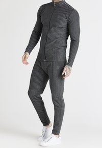 Stretch-fit sportset i mörkgrått med tunna vertikala ränder, långa ärmar, hög krage och byxor med elastisk midja.