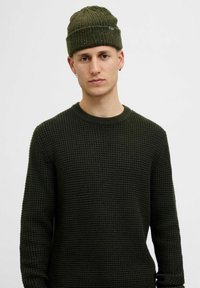 Mørkegrøn strikket sweater med et struktureret, vaffelmønster, parret med en matchende ribbet hue, der har subtile spraglede accenter.