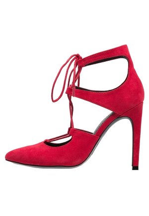 Czerwony zamszowy but na wysokim obcasie z ostrym czubkiem, wyciętymi bokami i sznurówką zawiązaną w kokardę wokół kostki.