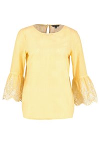 Gul blus med rutmönster, rund halsringning och utsvängda ärmar med floralt spetsband. Detalj med nyckelhål på ryggen synlig.