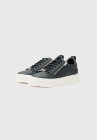 Sneaker mit einem strukturierten Obermaterial aus schwarzem Leder, ausgestattet mit einem seitlichen Reißverschluss, schwarzen Schnürsenkeln und einer dicken weißen Gummisohle.
