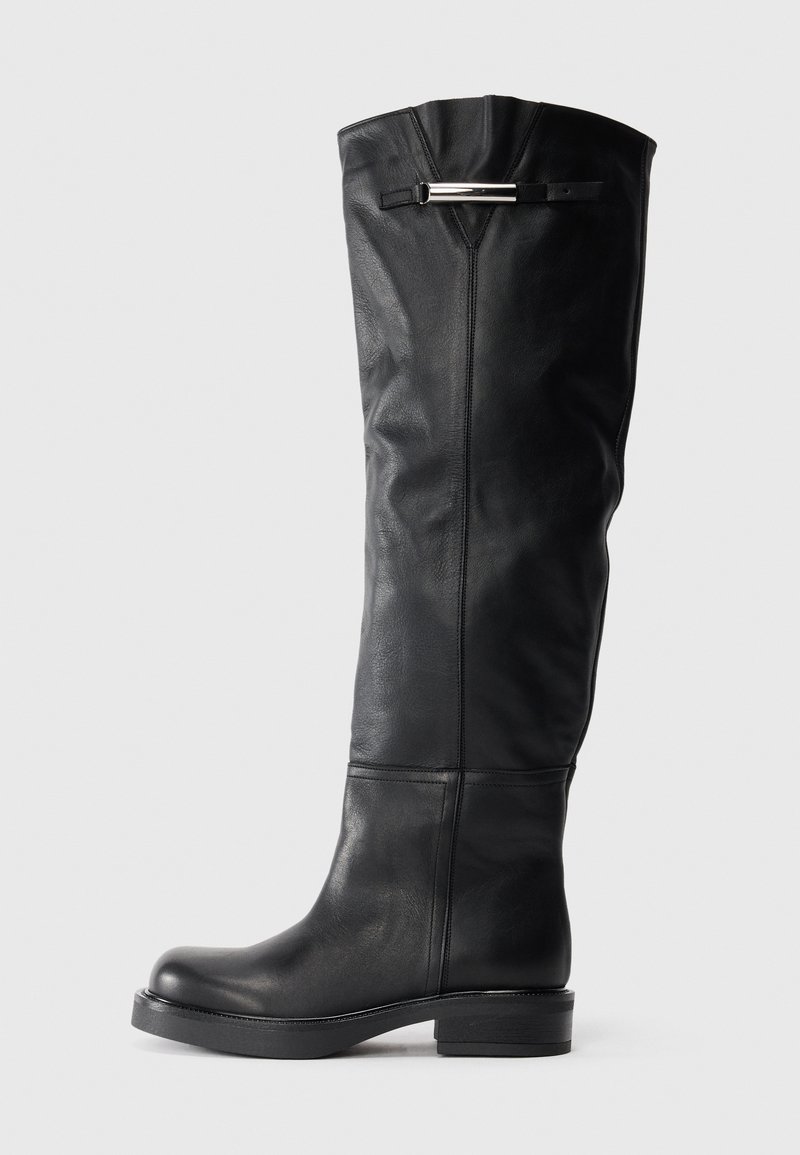 Botas de cuero negro hasta la rodilla con una textura suave, punta redondeada y un tacón bajo tipo bloque. Presentan un acento plateado en la parte superior.
