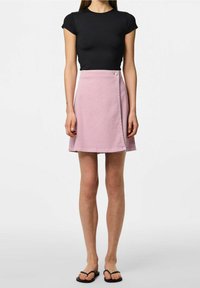 Rosa omlottkjol med en slät yta, med knappstängning och rak fåll, kombinerad med en svart tight t-shirt och svarta flip-flops.