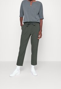 Grå blus med rund hals och trekvartslånga ärmar, kombinerad med mörkgröna figurformade byxor. Vita sneakers kompletterar outfiten.