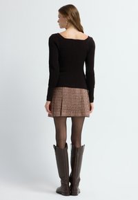 Vrouw die wegkijkt in een zwarte langmouwtop, een gestreepte korte rok, zwarte panty's en lange, donkerbruine leren laarzen.