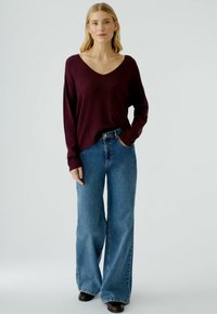 Burgunderfarbener gerippter Pullover mit weitem V-Ausschnitt, kombiniert mit hochtaillierten, locker sitzenden blauen Jeans und schwarzen Stiefeletten mit Absatz.