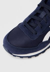 Navyblaue Sneaker mit Wildlederüberzügen, einem Mesh-Zehenbereich, schwarzen Schnürsenkeln, einem weißen Logostreifen und einer schwarz-weißen Gummisohle auf hellem Hintergrund.
