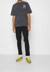 Mörkgrå oversized t-shirt med en färgglad solnedgångsgrafik, kombinerad med svarta cargobyxor och mångfärgade sneakers med kamouflagemönster.