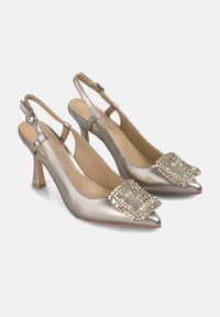 Talons slingback en argent métallisé avec des bouts pointus, une boucle décorative en bijoux, des talons effilés et une texture en cuir lisse.