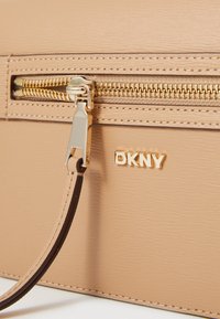 Borsa beige DKNY con finitura testurizzata, zip e hardware dorati; dotata di tracolla marrone rimovibile e logo del marchio in evidenza.