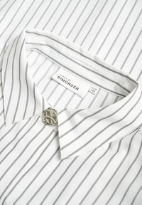 White shirt with thin black stripes, featuring a pointed collar and a decorative silver button at the neck. Label reads "KAREN BY SIMONSEN."