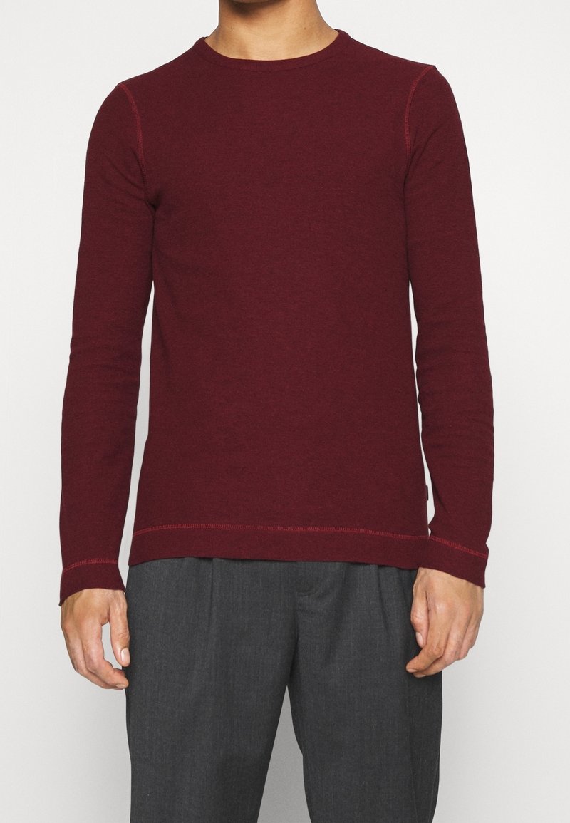 Bordowy sweter z długim rękawem z miękkiej dzianiny, z okrągłym dekoltem i kontrastującymi przeszyciami na ramionach i dole.