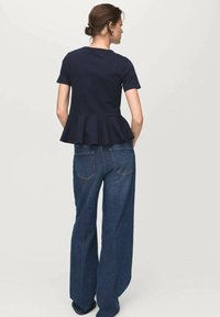 Top peplum blu con maniche corte abbinato a jeans in denim a vita alta e gamba larga. Tessuto dalla consistenza liscia e dettagli di design sottili.