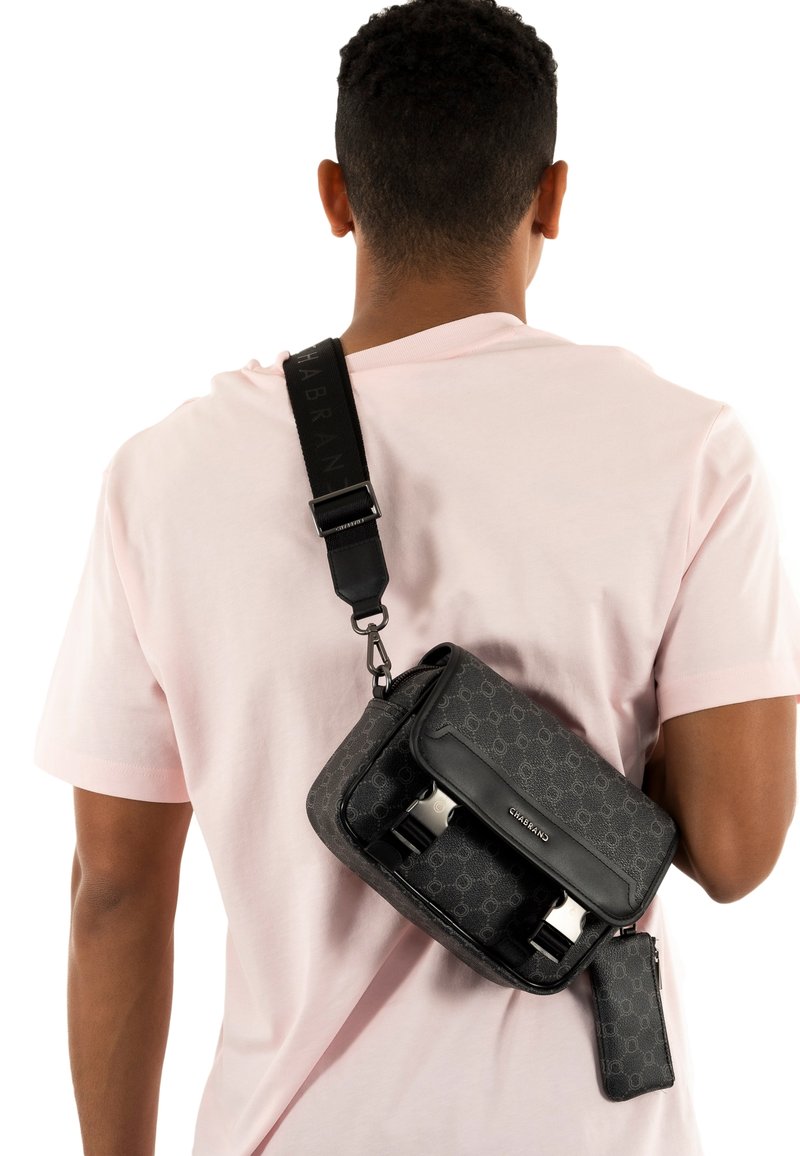 Sac bandoulière noir à motif, fabriqué dans un matériau élégant, avec un rabat supérieur, une bandoulière réglable et une petite pochette attachée.