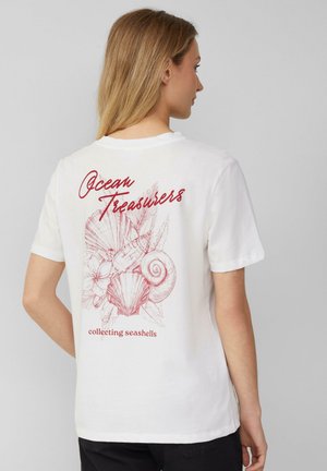 T-shirt en coton blanc avec un design graphique rouge de coquillages et de fleurs au dos, avec le texte "Trésors de l'océan" et "collection de coquillages".