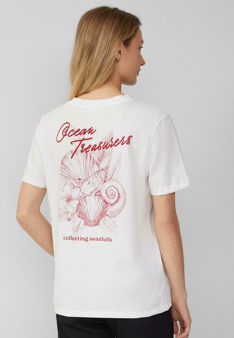 T-shirt en coton blanc avec un design graphique rouge de coquillages et de fleurs au dos, avec le texte "Trésors de l'océan" et "collection de coquillages".