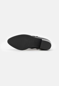 Suela de zapato negra con textura antideslizante, punta ligeramente redondeada y tacón plano. Presenta el nombre de la marca grabado cerca del tacón. Acabado de material liso.