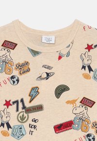 Beige short-sleeve t-shirt featuring various colorful patches, including dinosaurs, planets, and skateboarding themes, with a round neck design.