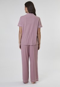 Top de pijama de manga corta en rosa claro con ribetes blancos, combinado con pantalones holgados a juego. Tejido suave y liso con un ajuste relajado.