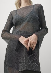 Třpytivý černý síťovaný top s dlouhým rukávem a zvonovými rukávy, doplněný třpytivou černou kabelkou zdobenou rhinestones.
