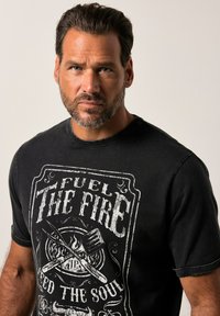 Czarna bawełniana koszulka z grafiką na przodzie, przedstawiającą napis "Fuel The Fire" oraz skrzyżowaną szpatułkę i widelec nad ilustracją ognia.