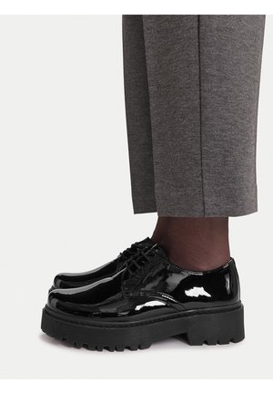 Czarne lakierowane buty ze skórzaną podeszwą na grubej podeszwie i zaokrąglonym noskiem. Zawiązywane na sznurowadła; szczegółowe przeszycia wzdłuż boków. Widoczne powyżej szare, zwężane spodnie.