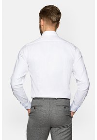 Biała koszula z długim rękawem o klasycznym kołnierzyku, gładkiej teksturze i mankietach zapinanych na guziki. Połączona z szarymi spodniami w kratę z tylnymi kieszeniami.