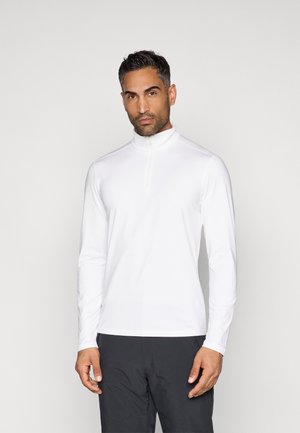 Långärmad vit sportskjorta med halvdraget krage, slät textur och åtsittande design, kombinerad med mörka byxor.