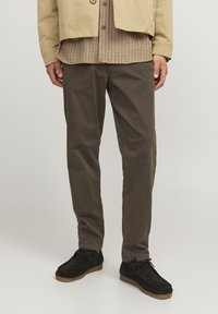 Khaki chinos with a relaxed fit, made of cotton, paired with black suede shoes featuring brown rubber soles and round laces.