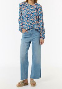 Blusa floral con fondo azul y flores rosas, combinada con jeans de pierna ancha de talle alto en azul claro y sandalias de esparto trenzadas en color beige.