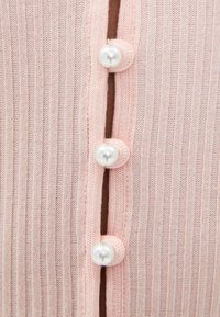 Tre pärlknappar knäppta på en ljusrosa ribbad stickad cardigan.