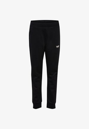 Barn iført sorte Hummel sportbukser og blå sneakers, stående mod en ensartet lys baggrund.