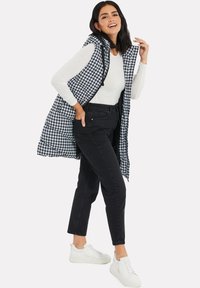 Svart och vit hounds-tooth lång väst med huva, bärs över en vit skjorta och svarta jeans, kombinerat med vita sneakers. Har sidofickor.