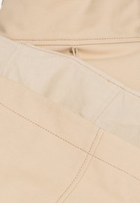 Tissu beige avec coutures visibles au niveau de la couture et bord plié montrant la doublure intérieure plus claire et une petite boucle en tissu.