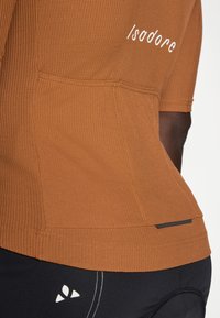 Mørkebrunt ribbet treningsgenser med korte ermer. Har hvitt logo og horisontale søm detaljer. Glatt tekstur gir stretch.
