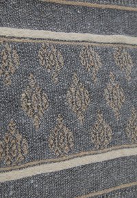 Tkanina o ciemnoszarym tle z misternymi złotymi wzorami. Poziome beżowe paski podkreślają wzór, dodając tekstury i głębi.