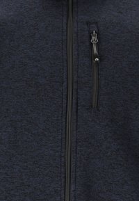 Laivaston sininen fleece-takkia, jossa on teksturoitu pinta, rintatasku ja musta vetoketju. Varustettu pienellä logolla vetoketjun vedin.