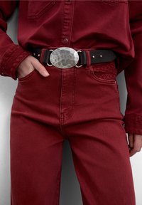 Cămașă și pantaloni din denim vișiniu, cu o curea texturată din piele neagră, având o cataramă ovală argintie bătută și cusături decorative.