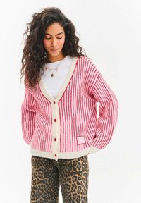 Růžový a bílý proužkovaný cardigan s texturou, výstřihem do V, červenými knoflíky a náprsní kapsou. Kombinován s kalhotami s leopardím potiskem.