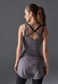 Grå atletisk tanktop med kryss bakstropper, kombinert med grå shorts. Glatt tekstur, tettsittende design, ingen synlige mønstre eller festemidler.
