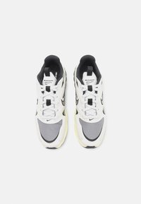 Vita och grå sportskor med en texturerad ovandel, svarta detaljer och en gul sula. Har snörning och en "Zoom Air"-logotyp på tungan.