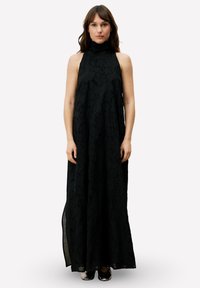 Zwarte maxijurk met een hoge hals, gemaakt van een gestructureerde stof met bloemmotieven. Losvallend ontwerp met dubbele splitten aan de zijkanten voor bewegingsvrijheid.