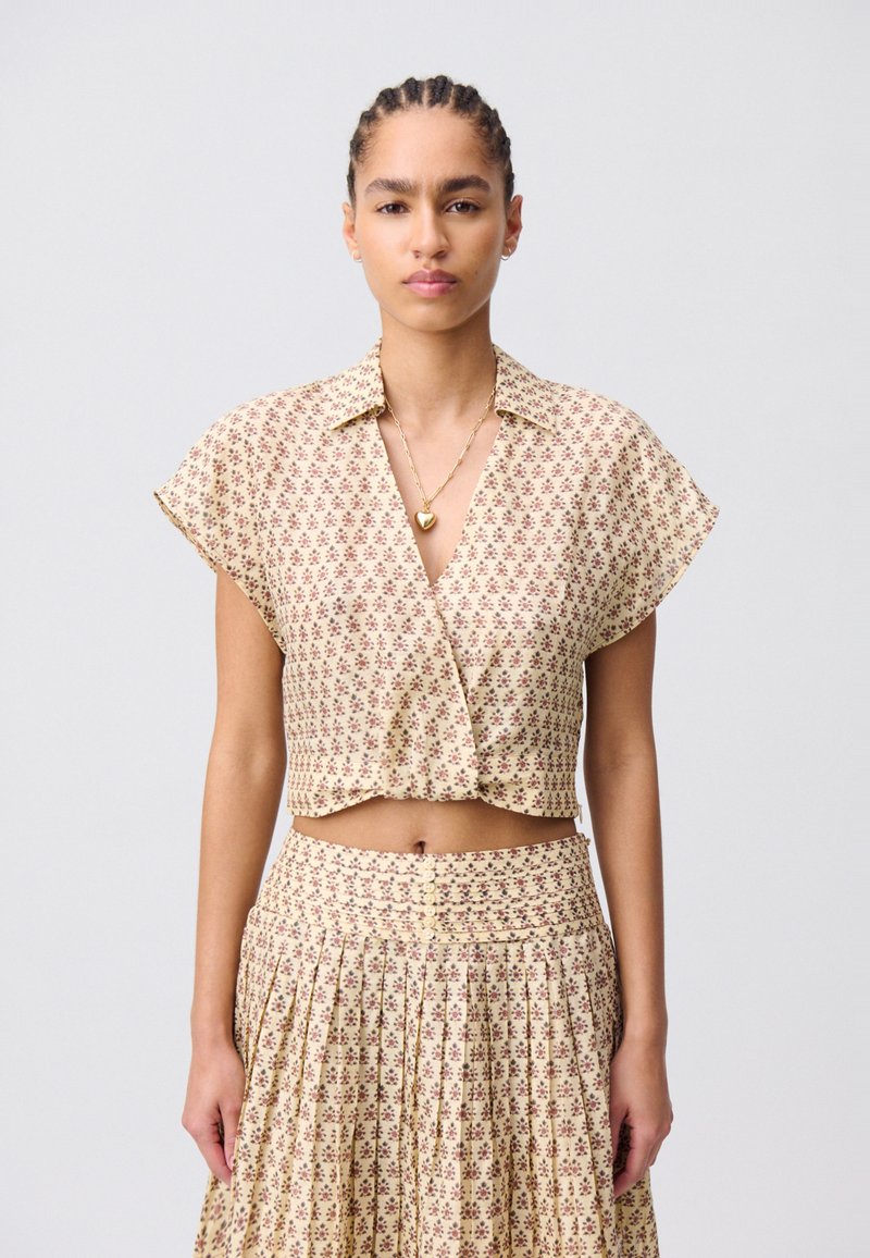 Blusa corta con motivo floreale in beige, con maniche corte e colletto, abbinata a una gonna plissettata coordinata. Texture liscia e dettagli con bottoni.