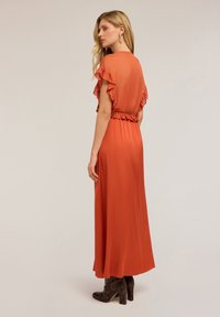 Vestido maxi en óxido con una espalda vaporosa y con volantes, y cintura elástica. Textura suave y una silueta fluida, combinado con botas con tacón y con estampado.