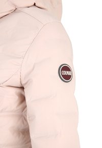 Une veste rembourrée rose clair avec une manche arborant un logo Colmar rond et bien visible en rouge et blanc, d'une texture lisse et légèrement brillante.